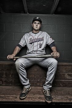 a baseball player sitting on top of a bench with a bat in his hand and wearing a uniform