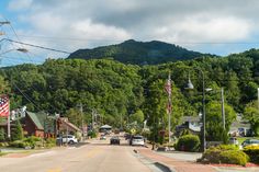 cars are driving down the street in front of some houses and trees with mountains in the background