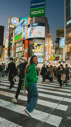 a woman walking across a cross walk in the middle of a busy city at night