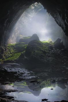 the inside of a cave with water and moss growing on the rocks in the foreground