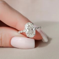 a woman's hand holding an oval diamond ring