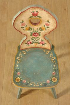 an old chair is sitting on the floor with flowers painted on it's back