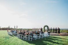 a group of people that are sitting in chairs on some grass and one person is standing at the end of the aisle