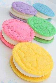 four cookies with different colored frosting are on a white surface, and one is in the shape of a cookie