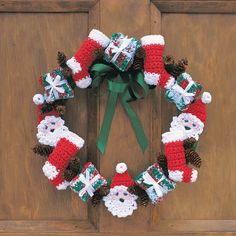 a knitted wreath with santa clause and pine cones hanging on a wooden door frame