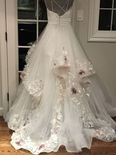 a wedding dress hanging up in front of a door with flowers all over the skirt