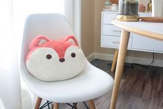 a white chair with a red fox pillow on it's back in front of a window