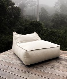 a white bean bag sitting on top of a wooden deck next to trees in the fog