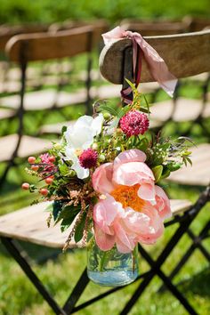 an arrangement of flowers in a vase sitting on a folding chair at a wedding ceremony