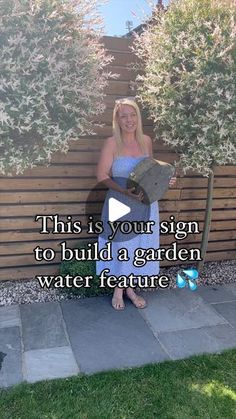 a woman in a blue dress standing next to a wooden fence and holding a book