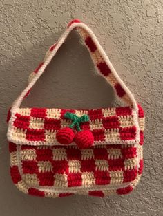 a crocheted purse hanging on the wall in front of a gray wall with white and red stripes