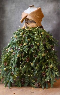 a dress made out of pine cones and evergreen needles with lights on the skirt is sitting on a wooden table