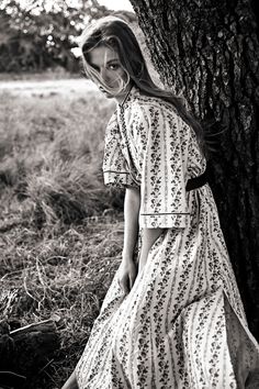 a woman leaning against a tree in a field