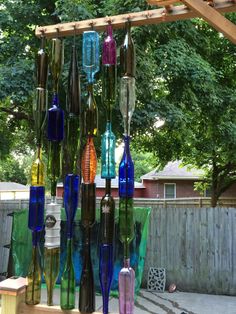 several different colored glass bottles are hanging from a wooden structure in front of a fence