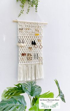 a macrame wall hanging next to a potted plant with earrings on it