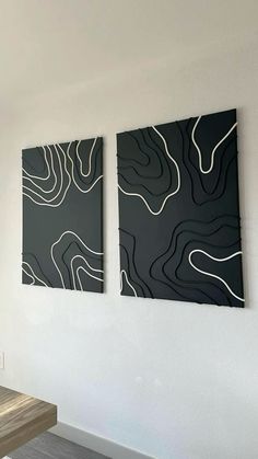 two black and white paintings hanging on the wall next to a wooden table in a room