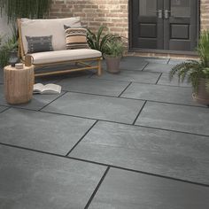 a couch sitting on top of a stone floor next to a planter and potted plants