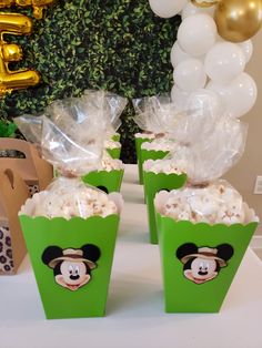 two green boxes filled with popcorn sitting on top of a table next to foil balloons