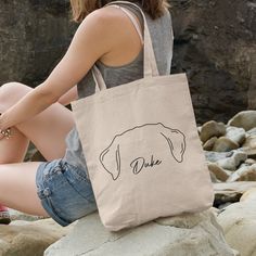 a woman sitting on rocks with a tote bag in front of her that says duke