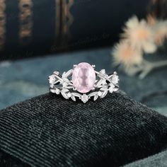 an oval pink stone surrounded by leaves sits on top of a black velvet cushion in front of a book