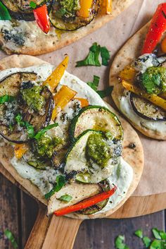 two pita breads topped with vegetables and sauce on a cutting board next to parsley