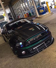 a black sports car parked in front of a gas station with its hood up and lights on