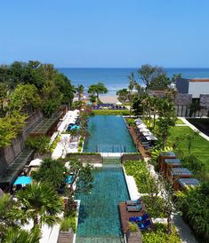 an outdoor swimming pool surrounded by trees and lawn chairs with the ocean in the background