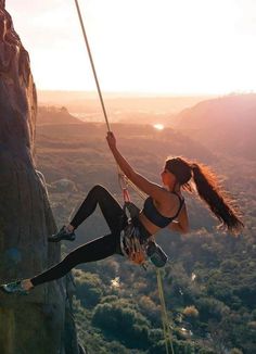 a woman climbing up the side of a cliff with her hands in the air while holding onto a rope