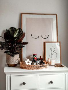 a white dresser topped with a potted plant next to a framed photograph and other items