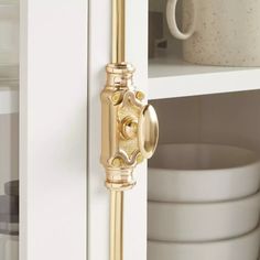 a close up of a door handle on a white cabinet with dishes in the background