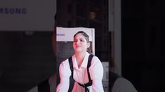 a woman wearing a pink shirt and black suspenders is standing in front of a samsung advertisement