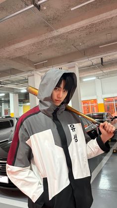 a man holding a baseball bat while standing next to a car in a parking garage