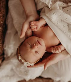 a woman holding a newborn baby wrapped in a white blanket on top of a wicker basket