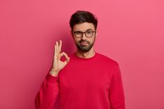 a man in a red sweater making the v sign with his fingers against a pink background