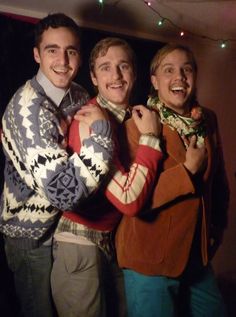 three young men standing next to each other in front of a christmas tree with lights