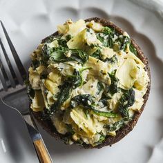 an open faced sandwich topped with spinach and cheese on a white plate next to a fork