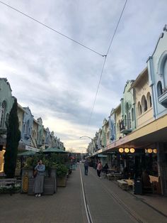 people are walking down the street in front of some buildings and shops on a cloudy day