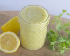 a glass jar filled with liquid next to lemons and parsley