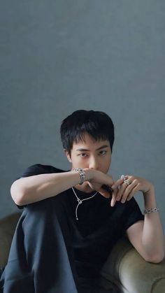 a young man sitting on top of a couch next to a white wall and holding his hand near his mouth