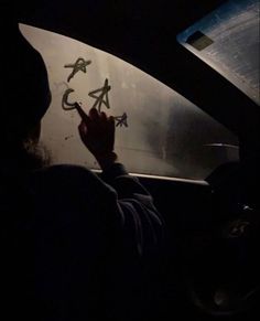 a person writing on the windshield of a car at night with their hand in the air