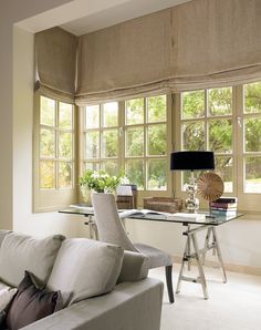 a living room filled with furniture and large windows covered in roman blind shades on top of them