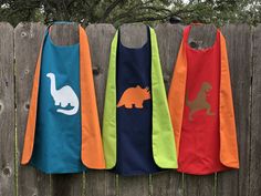 three bibs with dinosaurs on them hanging from a fence