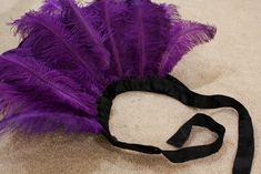 a purple feathered headband laying on top of a white surface with a black strap