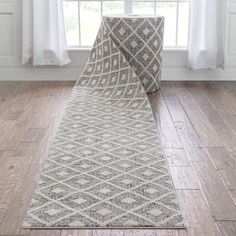 a white and gray rug sitting on top of a wooden floor next to a window