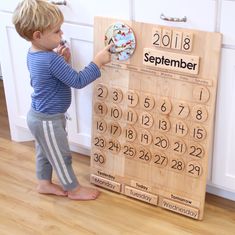 a little boy standing next to a wooden calendar