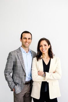 two people standing next to each other in front of a white wall with their arms crossed