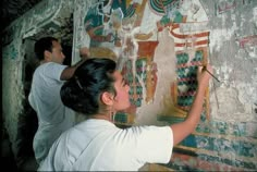 two men painting on a wall with colorful designs