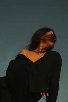 a woman with her hair blowing in the wind, wearing a black top and jeans