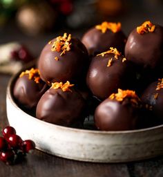 chocolate covered orange peels in a bowl with cranberries on the table next to it