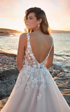 a woman in a wedding dress standing on the beach with her back to the camera